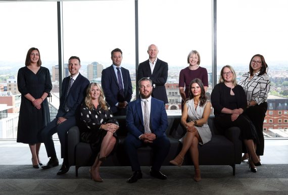 Posed group shot of lawyers in front of window with Belfast skyline in background